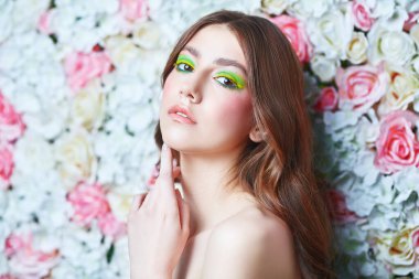 Bahar ve yaz güzelliği. Uzun dalgalı saçlı ve arkaplanda renkli makyajlı narin bir genç kadının portresi. Makyaj ve kozmetik.