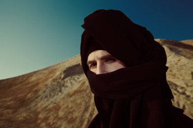 Siyah elbiseli ve başında siyah keffiyeh olan cesur genç bir adam çölde dikiliyor ve dalgın dalgın bakıyor. Maceralar, özgürlük ruhu.. 