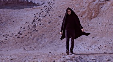 Siyah giysiler içinde çölde yürüyen yakışıklı bir esmer adamın tam boy portresi. Erkek modası. Özgürlük ve macera.