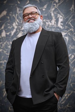 Gri sakallı ve gri saçlı yakışıklı bir adamın portresi grunge duvarda poz veriyor.. 