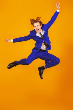 Zarif mavi takım elbiseli, zevkten dört köşe olmuş yakışıklı duygusal bir adamın portresi. Kopyalama alanı olan sarı arkaplan. Başarı konsepti. 