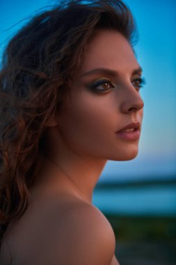 Güzel esmer bir kadının portresi, akşam gökyüzünün arka planına bakarak uzaklığı ölçüyor. Güzellik, makyaj.