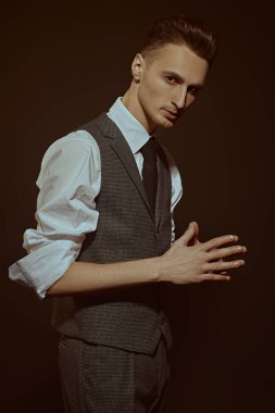 Zarif klasik takım elbiseli yakışıklı bir adamın portresi ve koyu kahverengi arka planda bir kravat. İş stili. Erkek modası.