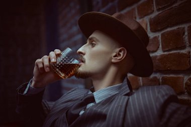 Yakışıklı sarhoş bir adam deri koltukta bir bardak viskiyle rahatça oturuyor. Lüks bir yaşam tarzı. Retro tarzı. Mafya ve suç dünyası. 