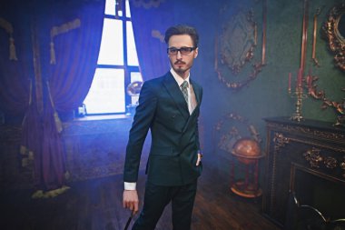 Lüks bir yaşam tarzı. Lüks bir dairede duran şık takım elbiseli yakışıklı bir adamın portresi. Erkek güzelliği, moda.