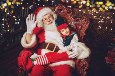 Nazik Noel Baba ve elfi evdeki koltukta dinleniyorlar. Noel ve Yeni Yıl masalları.