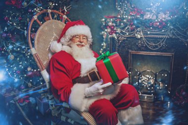Noel ve Yeni Yıl konsepti. Noel Baba Noel için hediyeler getirdi. Güzel bir Noel arifesinde bir koltukta oturuyor.. 