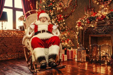 Neşeli Noel Baba güzel bir Noel evinde sallanan sandalyede sallanıyor. Noel ve Yeni Yıl Kutlaması. 