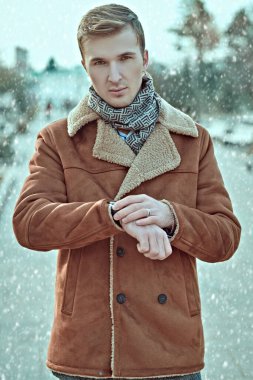 Koyun derisi ceketli yakışıklı genç adam kış parkında duruyor ve saatine bakıyor. Erkek aksesuarları.. 