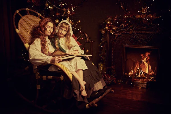 Christmas fairy tales. Happy mother tells fairy tales to her little daughter next to a beautiful fir tree on Christmas night. Vintage style.