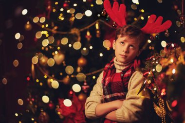 Geyik boynuzlu komik çocuk Noel süslemeleri içinde evde duruyor ve hayal kırıklığı içinde başını kaldırıyor. Noel ve Yeni Yıl kavramı. 