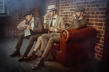 Erkek güzelliği, moda. Zarif takım elbiseli üç yakışıklı erkekler kulübünde puro ve viskiyle vakit geçiriyor. Lüks yaşam tarzı. 