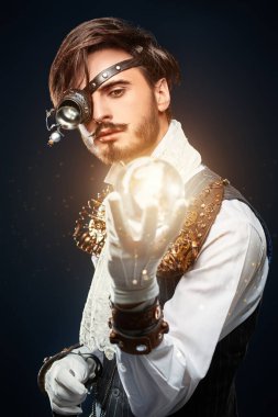 Tek gözlü kristal enerji topuna bakan yakışıklı bir steampunk adamın portresi. Koyu mavi arkaplan.  