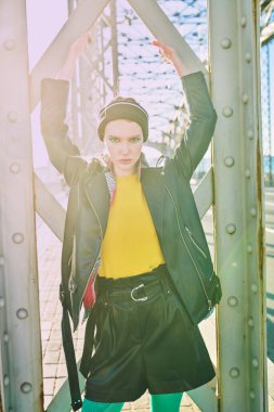 Parlak makyajlı modaya uygun bir kız büyük bir şehirde, bir köprüde şık ve renkli pozlar veriyor. Modaya uygun şehir tarzı.