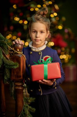 Zarif klasik okul üniforması içinde parlak ışıklarla dolu bir arka planda hediyeyle duran zeki bir kızın portresi. Noel ve Yeni Yıl.