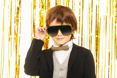 Parlak altın folyo perdelerle arka planda poz veren şık bir çocuk portresi. Çocuk modası ve tatiller. Çocuk partisi..