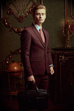 Klasik iç mimarisi olan lüks dairelerde poz veren resmi takım elbiseli yakışıklı bir gencin portresi. Erkek güzelliği, moda.