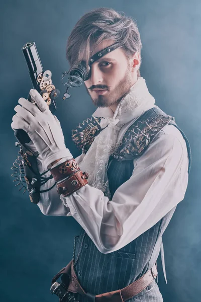 Steampunk man. Portrait of a handsome noble man with steampunk gadgets and a gun on a dark background with haze.