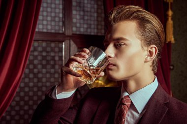 Lüks bir yaşam tarzı. Klasik takım elbiseli yakışıklı bir gencin portresi lüks dairelerde viski içiyor. Erkek güzelliği, moda.