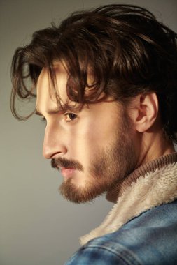 Erkek güzelliği ve saç stili. Gri arka planda dalgalı siyah saçlı ve sakallı yakışıklı bir adamın portresi.. 