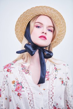 Hasır şapkalı güzel sarışın kız ve beyaz arka planda bir yaz bluzu. Pembe renkli açık renk makyaj. Bahar ve yaz güzelliği. Moda.. 