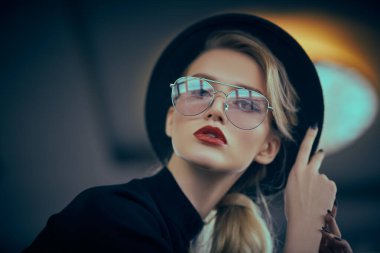Optik, gözlük. Modern gözlüklü ve iç mekan şapkalı şık bir genç kadının portresi. Güzellik, moda konsepti.  