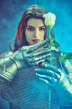 A beautiful and strong woman knight in armor holds a tender white rose in her iron gloves. Middle Ages. clipart