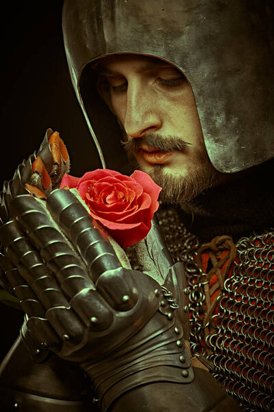 The era of romanticism. Close-up portrait of a noble knight in armor with a red rose in his hands.