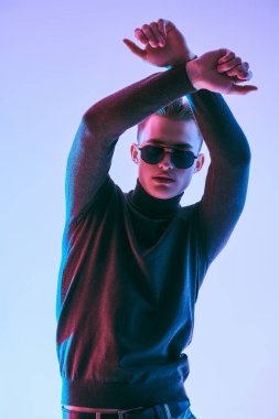 Moda fotoğrafı. Koyu gri kazaklı ve modern siyah güneş gözlüklü yakışıklı genç adam. Erkek aksesuarları, optikler. Stüdyo resmi.