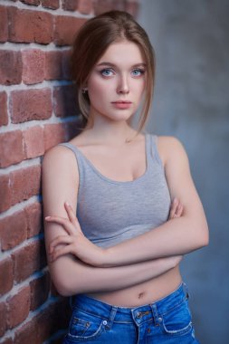 Kotlu güzel, ince bir kızın portresi ve tuğla duvara dayanmış spor bir bluz. Aktif yaşam tarzı. Güzellik, moda.