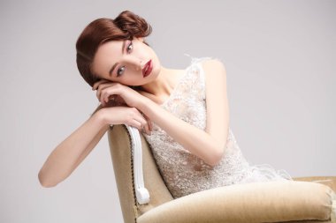 Lüks beyaz bir elbise içinde klasik koltukta poz veren güzel, şık bir kadının portresi. 20 'lerin akşam makyajı ve saç stili.. 