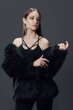 Stüdyoda siyah kıyafetler ve gri arka planda siyah kürklü poz veren çekici bir manken. Güzellik, moda.