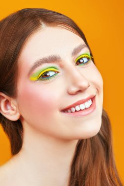 Parlak makyaj ve makyaj malzemeleri. Sarı arka planda parlak renkli makyajlı mutlu güzel bir kızın portresi.. 