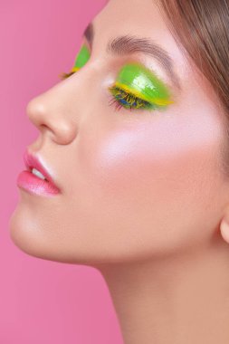 Makyaj ve makyaj malzemeleri. Pembe arka planda canlı yeşil ve sarı makyajlı güzel bir kadın yüzü.. 