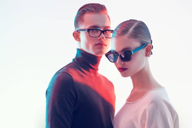 Moda stüdyosu çekimi. Yakışıklı genç adam ve güzel genç kadın şık gözlüklerle birlikte poz veriyorlar. Optik biçimi.