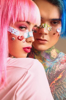 Çağdaş gençler. Parlak saçlı, dövmeli ve yüz çıkartmalı bir çift tutkulu genç. Anime tarzı.