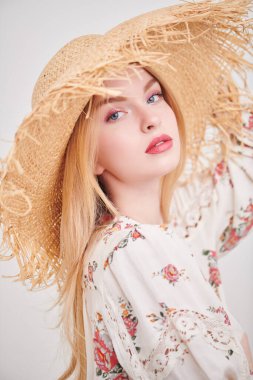 Bahar ve yaz güzelliği. Hasır şapkalı güzel sarışın kız ve beyaz arka planda bir yaz bluzu. Pembe renkli açık renk makyaj. Moda.. 