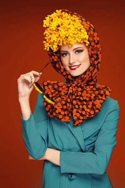 Portrait of a pretty woman model posing in fashionable elegant clothes and with mimosa flowers on her head and glasses. Bright saturated colors. Pin-up style.