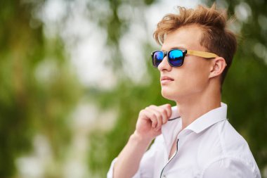 Yakışıklı genç adam parkta yürüyor ve gülümsüyor. Yaz modası. Yaz tatili ve tatil.