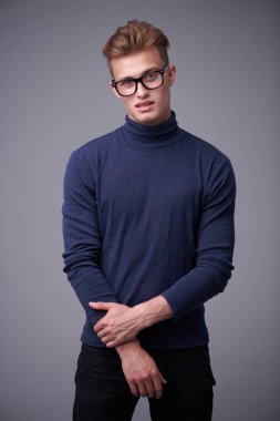 Gözlüklü yakışıklı sarışın adam kameraya şüpheyle bakıyor. Gri arkaplanda stüdyo portresi.