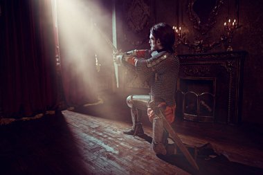 Zırhlı asil şövalye diz çöktü ve kaledeki ışığa bakarak kılıcını kaldırdı. Aşk.. 