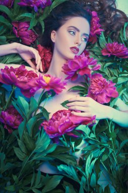 Parfüm ve güzellik ürünleri. Şakayık çiçeklerin arasında uzanan parlak makyajlı güzel esmer bir kadının portresi.. 