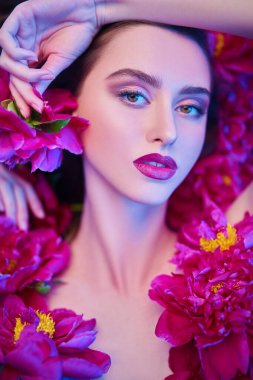 Parlak makyaj. Kozmetik ve parfüm. Şakayık çiçeklerin arasında uzanan parlak makyajlı güzel esmer bir kadının portresi.. 