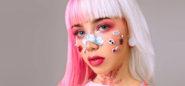 Pembe ve beyaz saçlı, parlak makyajlı, çıkartmalı ve yüzünde dekoratif yapıştırıcı olan modern bir genç kız. Anime tarzı.  