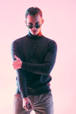 Erkek aksesuarları, optikler. Koyu gri kazaklı ve modern siyah güneş gözlüklü yakışıklı genç adam. Stüdyo resmi.