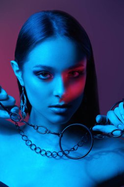 Güzellik, moda konsepti. Renkli ışıkta poz veren çekici esmer bir kızın portresi. Makyaj, makyaj malzemeleri, mücevherler. Stüdyo çekimi.