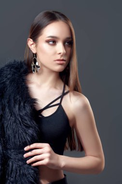 Stüdyoda siyah kıyafetler ve gri arka planda siyah kürkle poz veren çekici bir manken. Güzellik, moda.