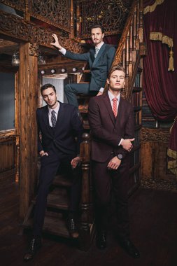 Klasik takım elbiseli üç yakışıklı adamın portresi. Klasik iç mimarisi olan lüks dairelerde poz veriyorlar. Erkek güzelliği, moda.