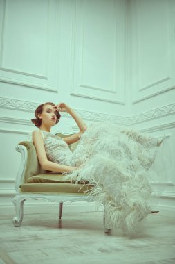 Beyaz bir odada klasik bir iç mimariye sahip beyaz elbiseli çarpıcı genç bir kadının tam boy portresi. Moda fotoğrafı. Gelinlik.