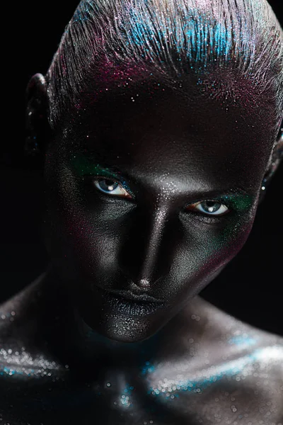 Beauty art portrait. High fashion model woman with black painted skin and sparkling glitter makeup posing in dark light. Makeup and cosmetics.